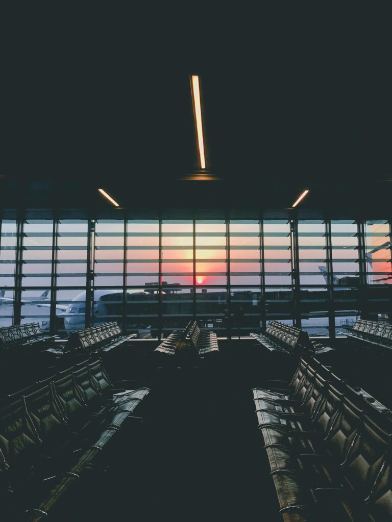 A serene view of an empty airport terminal during sunset, overlooking parked airplanes through large windows.